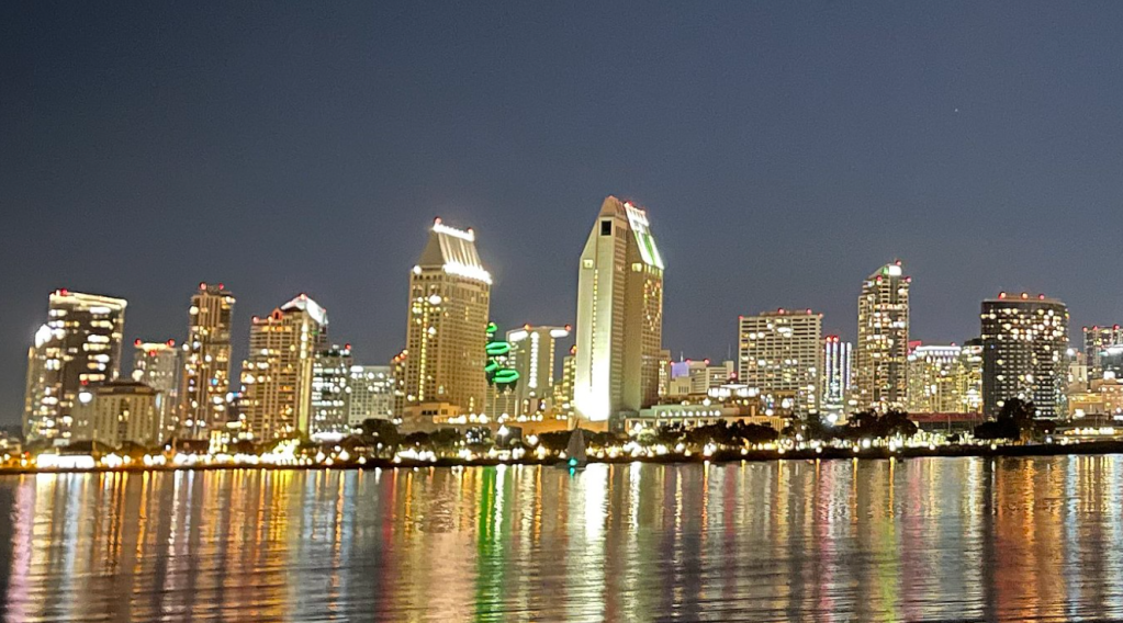 San Diego's skyline at night. Several tall buildings reflect light onto the bay.